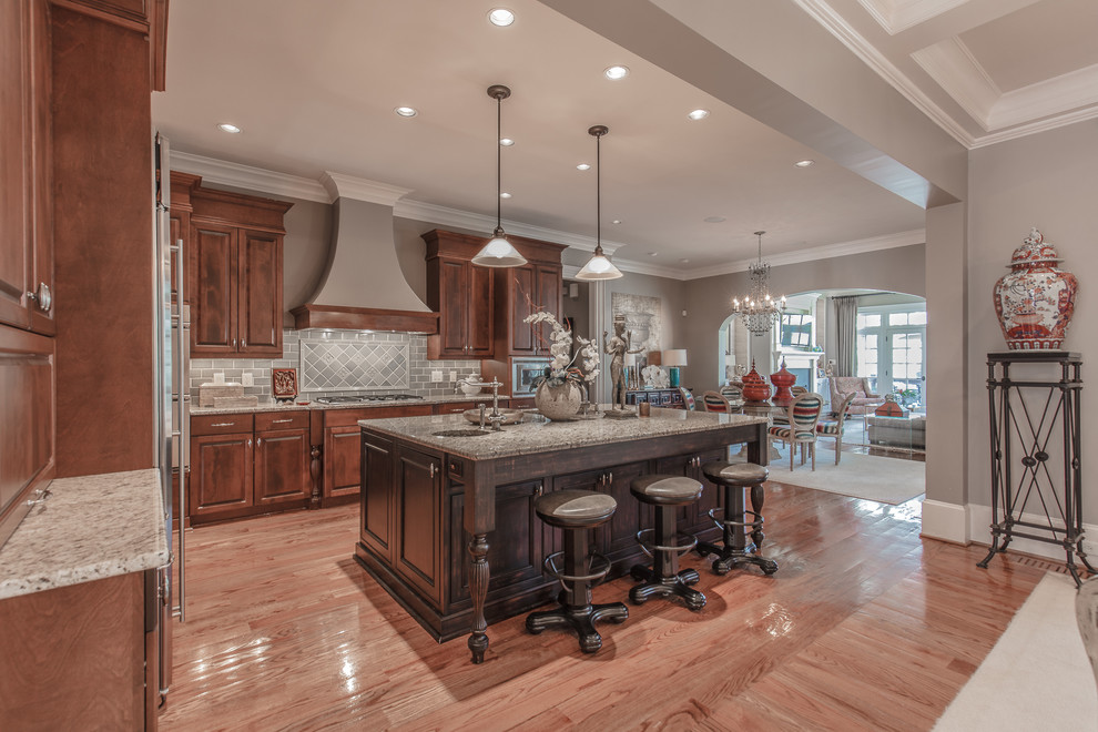 Traditional l-shaped kitchen in DC Metro with raised-panel cabinets, dark wood cabinets, medium hardwood floors, with island, brown floor and grey benchtop.