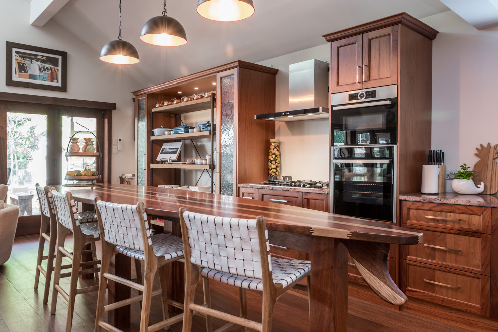 This is an example of a beach style galley kitchen in Other with recessed-panel cabinets, medium wood cabinets, stainless steel appliances, medium hardwood floors, with island, brown floor and brown benchtop.