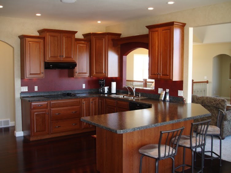 Large u-shaped dark wood floor eat-in kitchen photo with a drop-in sink, raised-panel cabinets, medium tone wood cabinets, laminate countertops, black appliances and an island