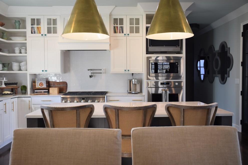 Large transitional dark wood floor eat-in kitchen photo with a farmhouse sink, shaker cabinets, white cabinets, quartzite countertops, white backsplash, subway tile backsplash, stainless steel appliances and an island