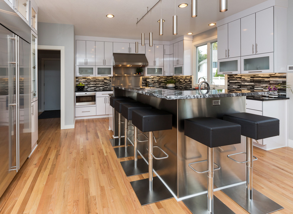 Large trendy u-shaped light wood floor open concept kitchen photo with an undermount sink, flat-panel cabinets, white cabinets, granite countertops, multicolored backsplash, mosaic tile backsplash, stainless steel appliances and an island