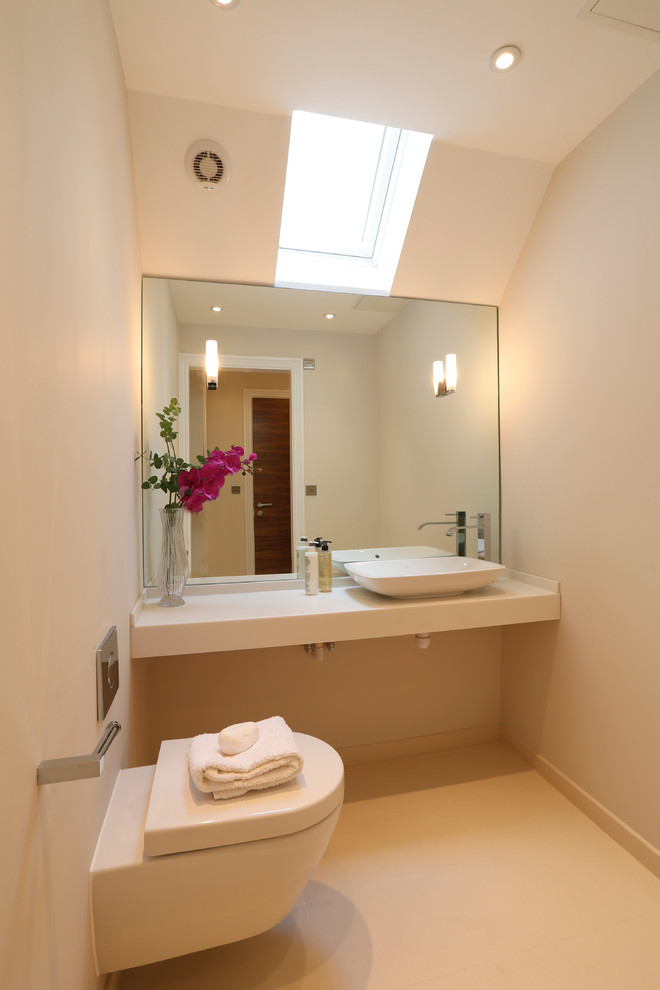 This is an example of a large contemporary powder room in London with solid surface benchtops, a wall-mount toilet, beige tile, porcelain floors, beige walls and a vessel sink.