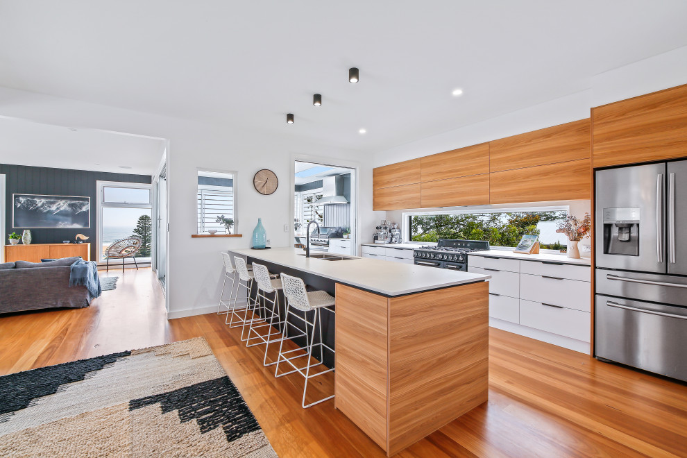 Design ideas for a large beach style galley open plan kitchen in Central Coast with an undermount sink, flat-panel cabinets, medium wood cabinets, mirror splashback, stainless steel appliances, a peninsula, brown floor and white benchtop.