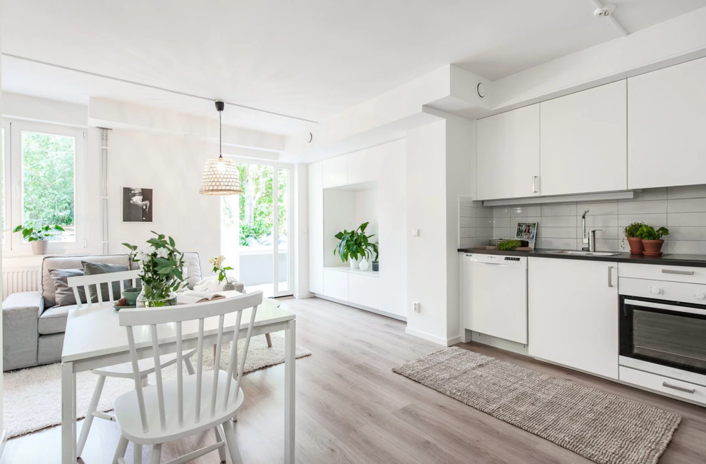 Small scandinavian single-wall open plan kitchen in Stockholm with flat-panel cabinets, white cabinets, laminate benchtops, white splashback, porcelain splashback, white appliances and grey benchtop.