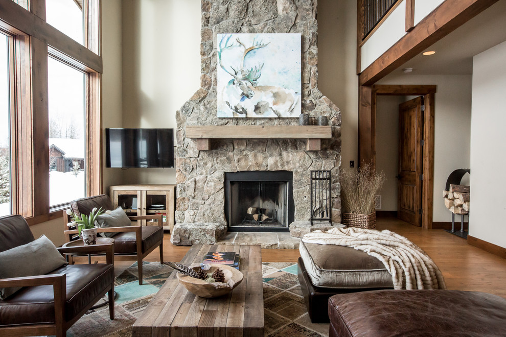 Large country formal enclosed living room in Other with beige walls, medium hardwood floors, a standard fireplace, a stone fireplace surround, a wall-mounted tv and brown floor.