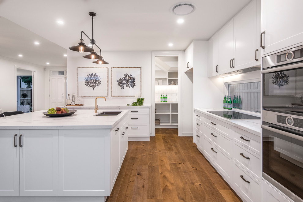 Design ideas for a large transitional kitchen in Brisbane with a double-bowl sink, white cabinets, marble benchtops, stainless steel appliances, medium hardwood floors, brown floor, white benchtop, shaker cabinets, window splashback and with island.