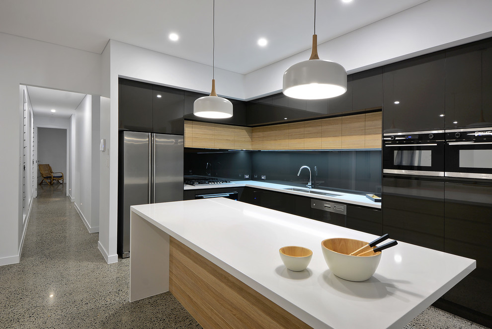 Inspiration for a contemporary l-shaped kitchen in Sunshine Coast with a double-bowl sink, flat-panel cabinets, black cabinets, black splashback, glass sheet splashback, black appliances, concrete floors, with island, grey floor and white benchtop.