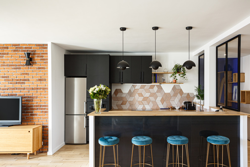 Modern inredning av ett mellanstort beige beige kök, med en enkel diskho, släta luckor, svarta skåp, träbänkskiva, orange stänkskydd, stänkskydd i keramik, svarta vitvaror, ljust trägolv, en köksö och beiget golv