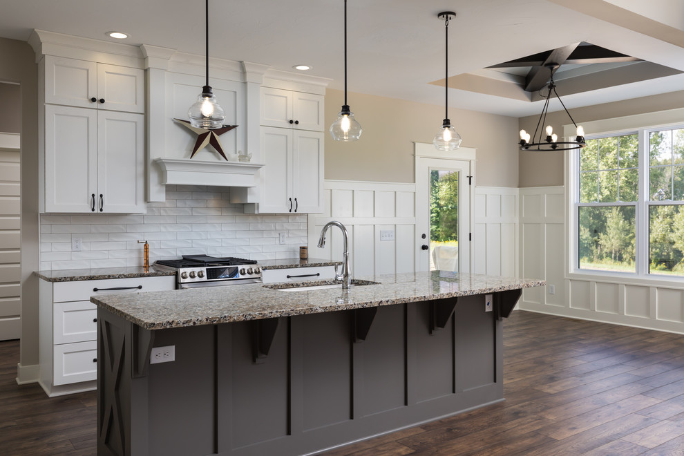 This is an example of a mid-sized traditional galley eat-in kitchen in Grand Rapids with a farmhouse sink, recessed-panel cabinets, white cabinets, granite benchtops, white splashback, subway tile splashback, stainless steel appliances, laminate floors, with island, brown floor and beige benchtop.