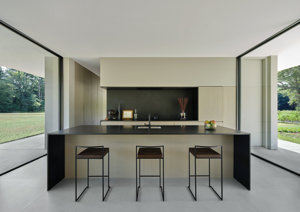 This is an example of a mid-sized modern galley open plan kitchen in Boston with an undermount sink, flat-panel cabinets, beige cabinets, black splashback, panelled appliances, porcelain floors, with island, grey floor and black benchtop.