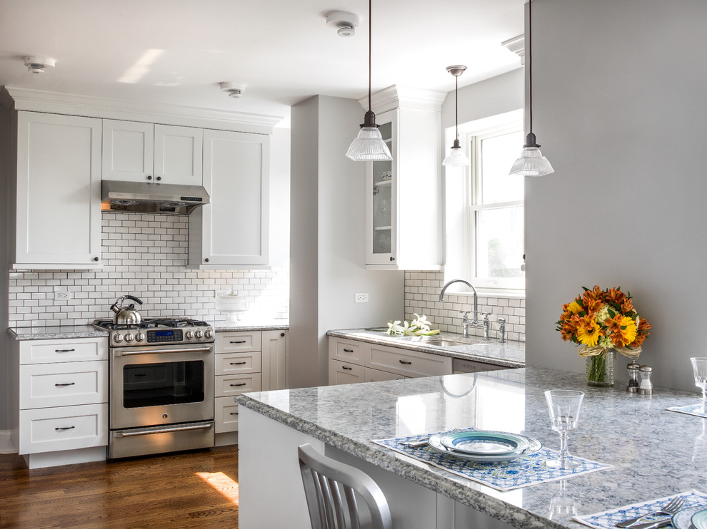 Photo of a traditional u-shaped kitchen in Chicago with an undermount sink, recessed-panel cabinets, white cabinets, white splashback, subway tile splashback, dark hardwood floors and a peninsula.