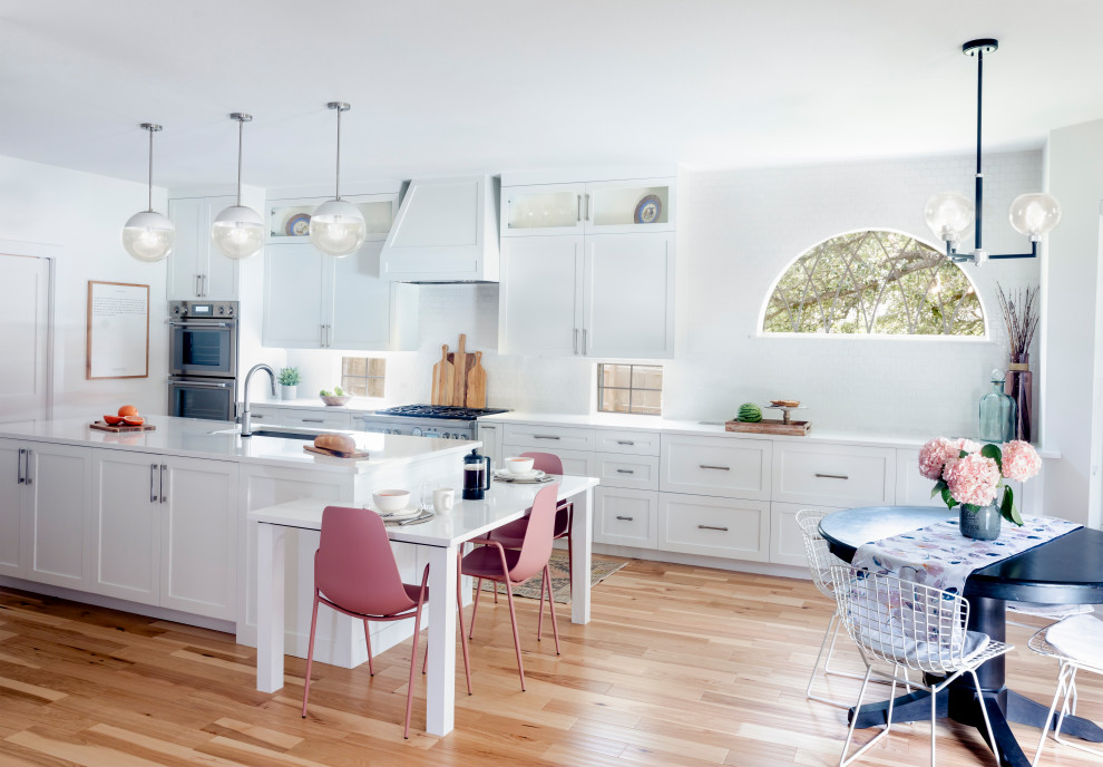 Eat-in kitchen - large transitional l-shaped light wood floor and brown floor eat-in kitchen idea in Austin with a single-bowl sink, shaker cabinets, white cabinets, quartz countertops, white backsplash, ceramic backsplash, stainless steel appliances, an island and white countertops