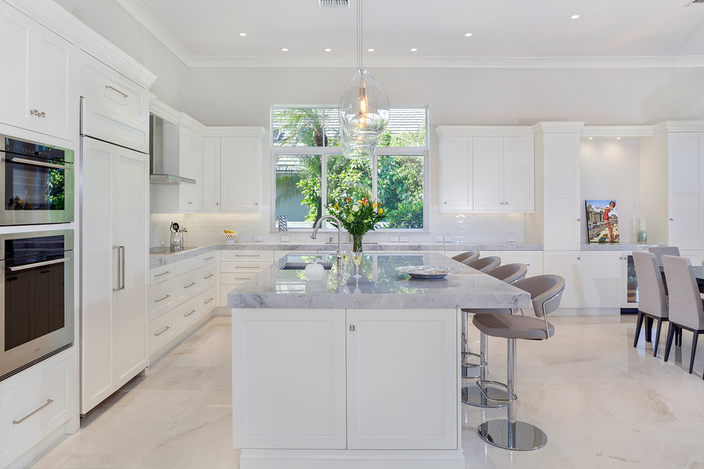 Example of a large transitional galley marble floor and beige floor eat-in kitchen design in Miami with a drop-in sink, recessed-panel cabinets, white cabinets, marble countertops, white backsplash, glass tile backsplash, stainless steel appliances, an island and gray countertops