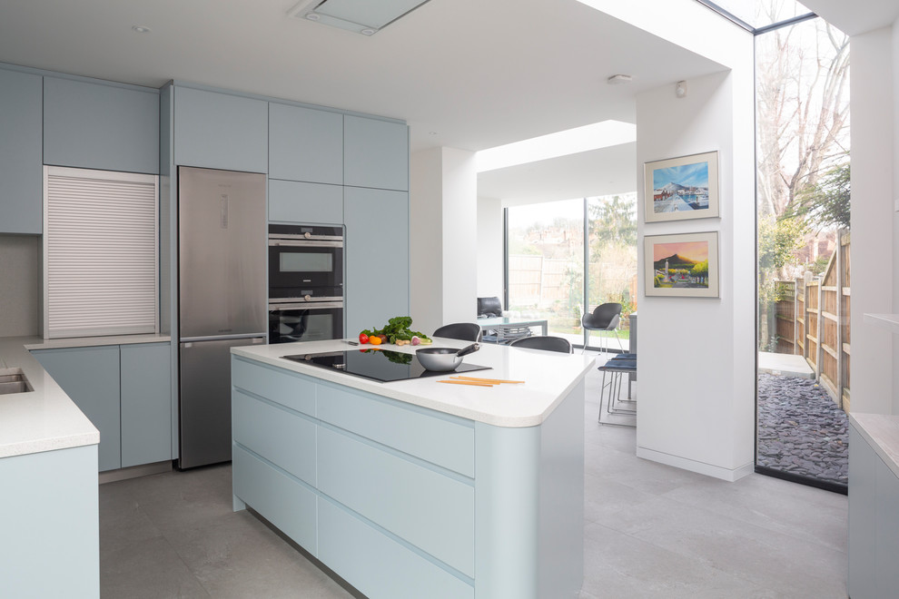 Photo of a mid-sized contemporary open plan kitchen in London with flat-panel cabinets, blue cabinets, black appliances, with island and white benchtop.