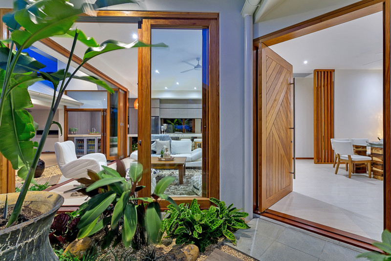 This is an example of a small tropical front door in Cairns with white walls, porcelain floors, a pivot front door and a medium wood front door.
