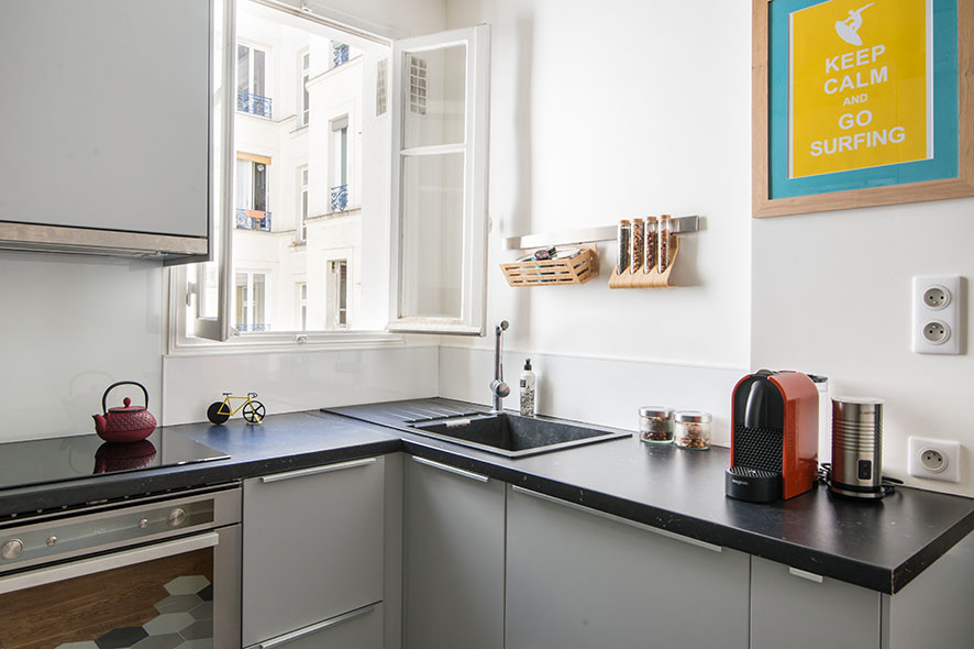 Cette image montre cuisine ouverte in U With un évier 1 bac, des portes de placard grises, un plan de travail en stratifié, une crédence blanche, une crédence en carreau de verre, un sol en carrelage de porcelaine, un sol gris and plan de travail noir.