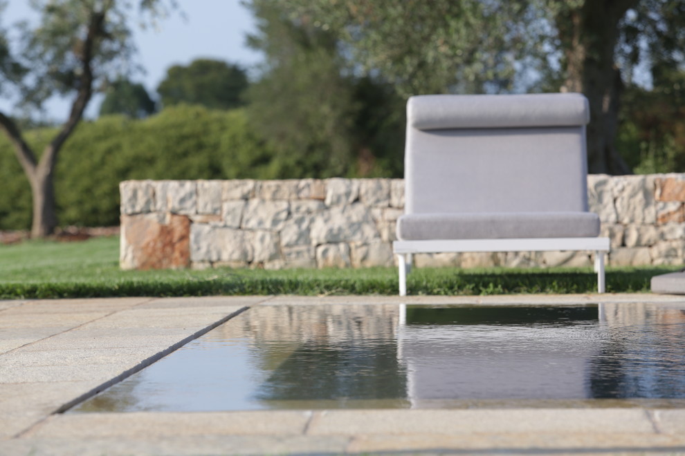 Mid-sized country backyard rectangular infinity pool in Bari with natural stone pavers.