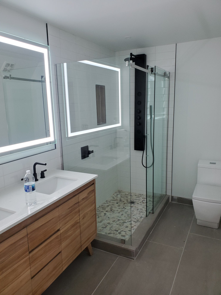 Mid-sized contemporary master bathroom in Indianapolis with flat-panel cabinets, medium wood cabinets, an alcove shower, a one-piece toilet, white tile, ceramic tile, white walls, ceramic floors, an integrated sink, engineered quartz benchtops, grey floor, a sliding shower screen, white benchtops, a double vanity and a freestanding vanity.