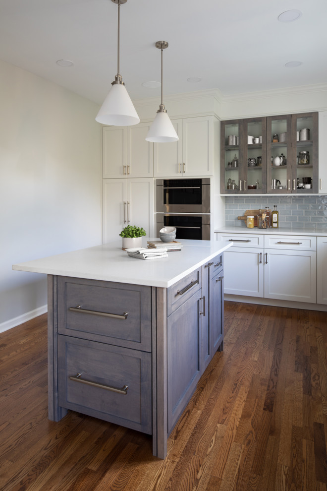 Mid-sized transitional l-shaped medium tone wood floor and brown floor enclosed kitchen photo with an undermount sink, shaker cabinets, white cabinets, quartz countertops, blue backsplash, subway tile backsplash, stainless steel appliances, an island and white countertops