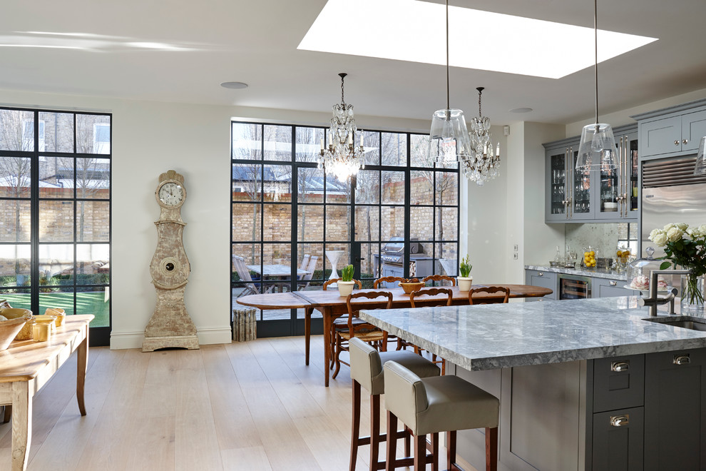 Large traditional l-shaped eat-in kitchen in London with an undermount sink, recessed-panel cabinets, blue cabinets, marble benchtops, metallic splashback, glass sheet splashback, light hardwood floors and with island.