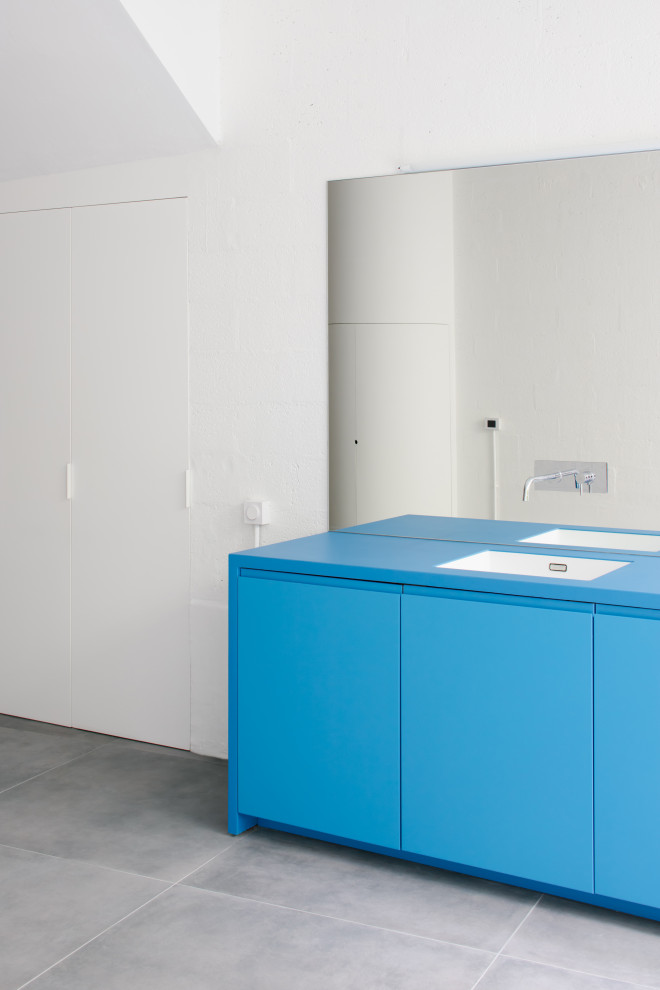 Foto di una cucina minimalista di medie dimensioni con lavello sottopiano, ante lisce, ante blu, top in superficie solida, paraspruzzi a specchio, elettrodomestici da incasso, pavimento con piastrelle in ceramica, pavimento grigio, top blu e travi a vista