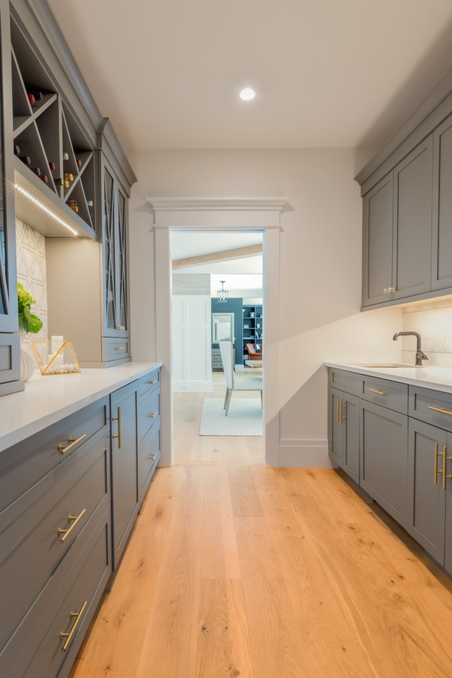 This is an example of a mid-sized beach style galley kitchen pantry in Boston with an undermount sink, shaker cabinets, grey cabinets, beige floor and white benchtop.