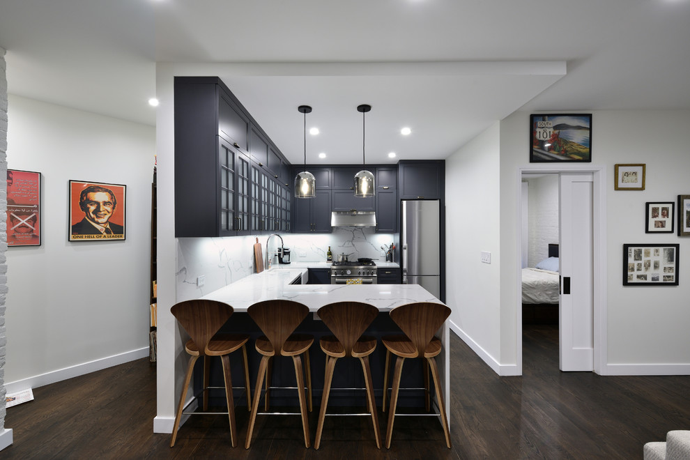 Design ideas for a transitional u-shaped kitchen in New York with a farmhouse sink, recessed-panel cabinets, black cabinets, white splashback, stone slab splashback, stainless steel appliances, dark hardwood floors, a peninsula, brown floor and white benchtop.