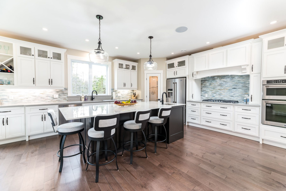 Mid-sized transitional medium tone wood floor and brown floor open concept kitchen photo with an undermount sink, shaker cabinets, white cabinets, granite countertops, gray backsplash, mosaic tile backsplash, stainless steel appliances, an island and gray countertops