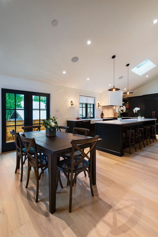 Example of a mid-sized mountain style l-shaped light wood floor and beige floor open concept kitchen design in Vancouver with a farmhouse sink, shaker cabinets, black cabinets, quartz countertops, paneled appliances, an island and white countertops