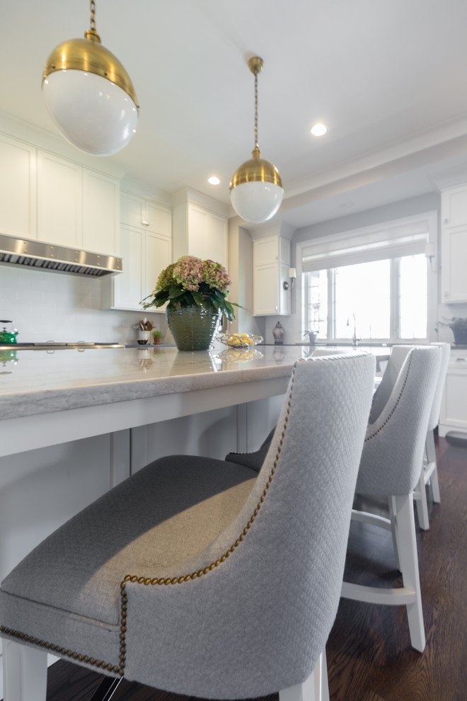 Example of a large transitional u-shaped dark wood floor and brown floor kitchen design in Chicago with an undermount sink, shaker cabinets, white cabinets, solid surface countertops, white backsplash, ceramic backsplash, stainless steel appliances, an island and black countertops