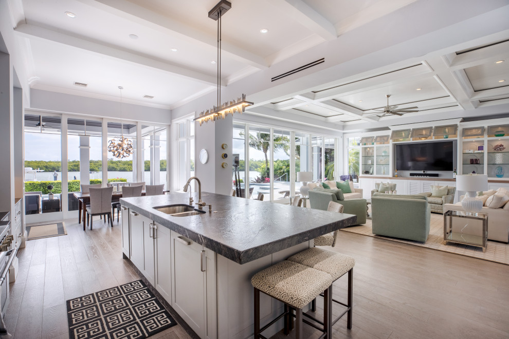 Beach style l-shaped open plan kitchen in Other with a double-bowl sink, flat-panel cabinets, white cabinets, stainless steel appliances, medium hardwood floors, with island, black benchtop and coffered.