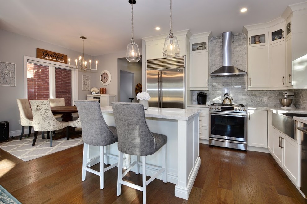 Inspiration for a mid-sized transitional l-shaped medium tone wood floor and brown floor eat-in kitchen remodel in Toronto with a farmhouse sink, shaker cabinets, white cabinets, quartz countertops, gray backsplash, marble backsplash, stainless steel appliances, an island and white countertops