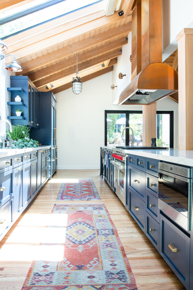 Photo of a transitional galley kitchen in Los Angeles with shaker cabinets, blue cabinets, stainless steel appliances, light hardwood floors, white benchtop and with island.