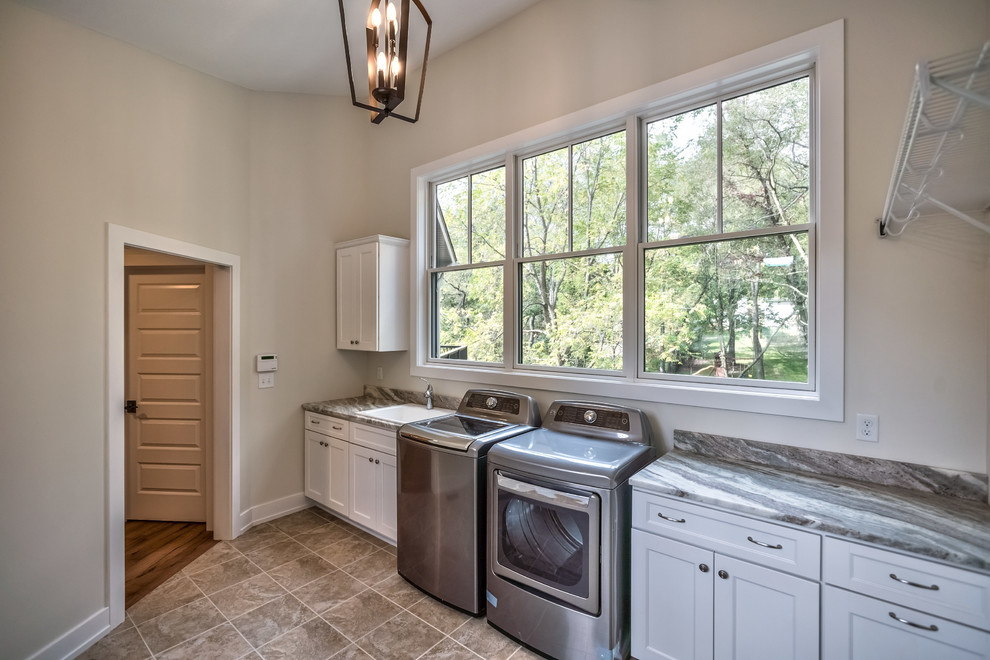 Design ideas for a large arts and crafts single-wall dedicated laundry room in Other with a drop-in sink, recessed-panel cabinets, white cabinets, soapstone benchtops, grey walls, ceramic floors, a side-by-side washer and dryer and brown floor.
