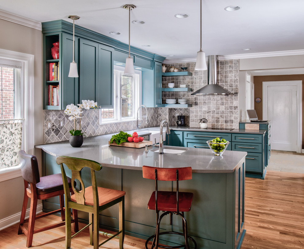Mid-sized traditional u-shaped eat-in kitchen in Indianapolis with a farmhouse sink, shaker cabinets, turquoise cabinets, quartz benchtops, grey splashback, stone tile splashback, stainless steel appliances, light hardwood floors and a peninsula.