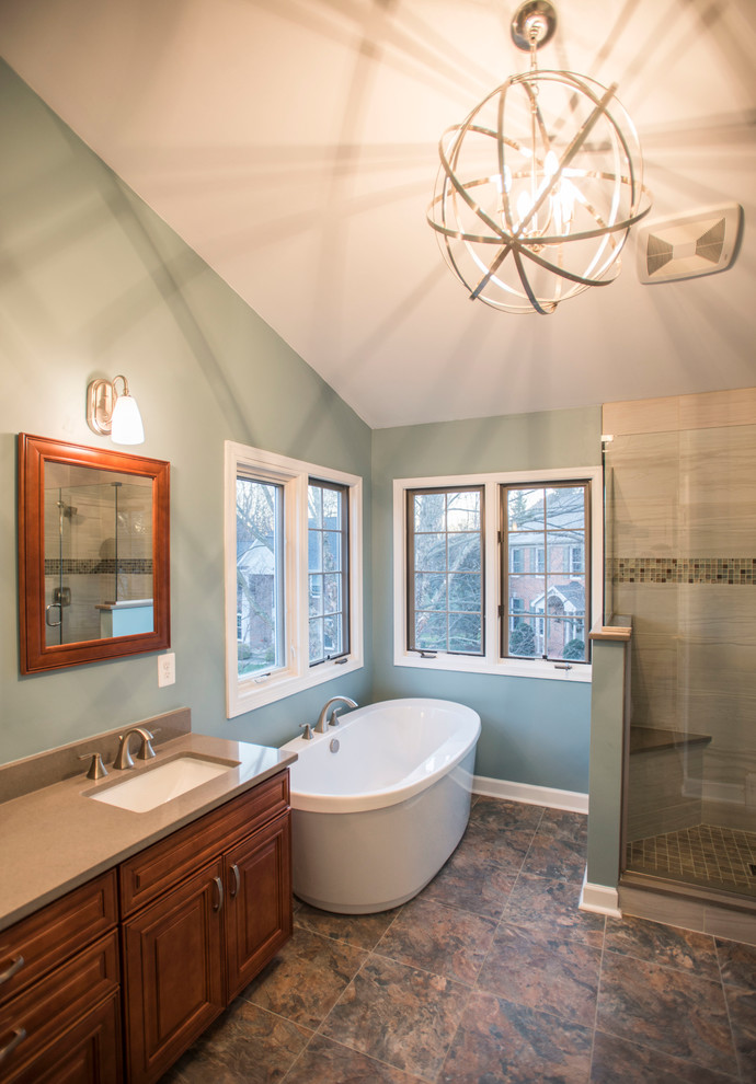 This is an example of a large transitional master bathroom in Baltimore with raised-panel cabinets, light wood cabinets, a freestanding tub, a corner shower, red tile, porcelain tile, blue walls, vinyl floors, engineered quartz benchtops, a one-piece toilet, a drop-in sink, multi-coloured floor and a hinged shower door.
