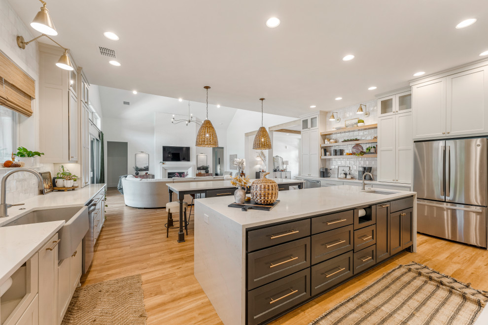 Example of a mid-sized transitional u-shaped light wood floor open concept kitchen design in Dallas with a farmhouse sink, shaker cabinets, gray cabinets, quartz countertops, white backsplash, porcelain backsplash, stainless steel appliances, two islands and white countertops
