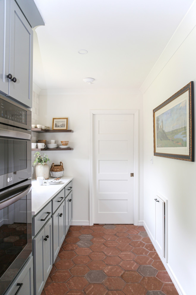 Idéer för att renovera ett avskilt, mellanstort retro vit vitt l-kök, med en rustik diskho, skåp i shakerstil, blå skåp, bänkskiva i kvarts, vitt stänkskydd, stänkskydd i porslinskakel, svarta vitvaror, klinkergolv i terrakotta, en köksö och rött golv