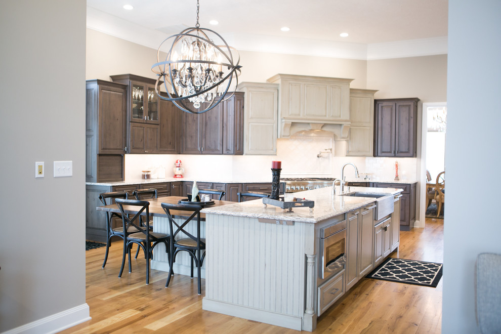 Example of a large transitional u-shaped medium tone wood floor and brown floor kitchen design in Indianapolis with a farmhouse sink, raised-panel cabinets, dark wood cabinets, granite countertops, white backsplash, subway tile backsplash, paneled appliances, an island and multicolored countertops