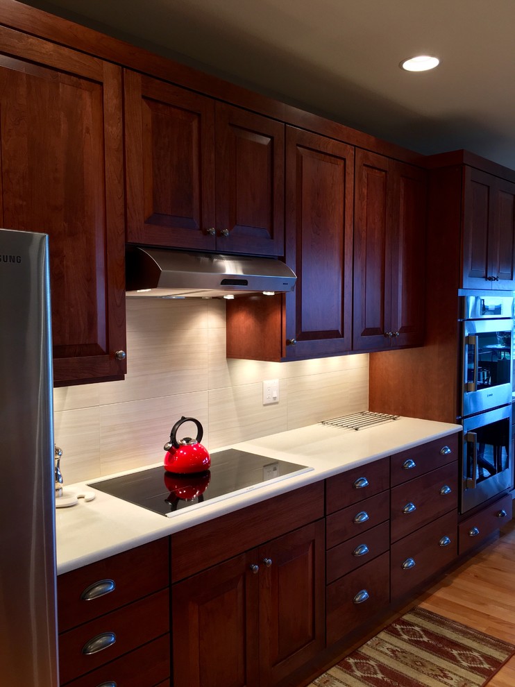 This is an example of a kitchen in Denver with an undermount sink, raised-panel cabinets, quartz benchtops, beige splashback, ceramic splashback, stainless steel appliances and medium hardwood floors.