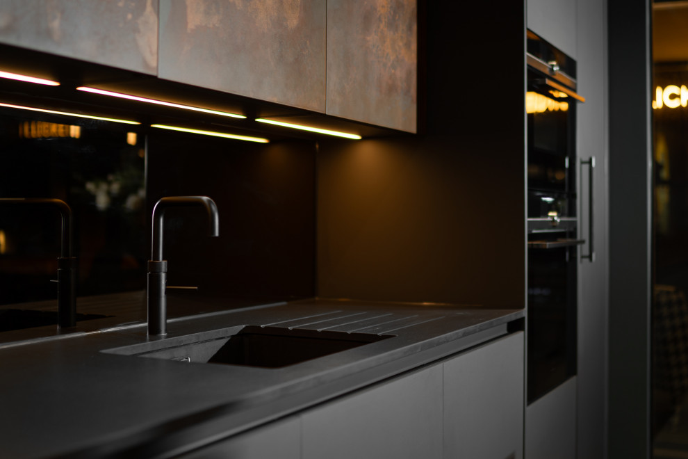 Idéer för att renovera ett mellanstort industriellt svart linjärt svart kök med öppen planlösning, med en integrerad diskho, släta luckor, skåp i slitet trä, bänkskiva i koppar, spegel som stänkskydd, svarta vitvaror, betonggolv, en köksö och grått golv