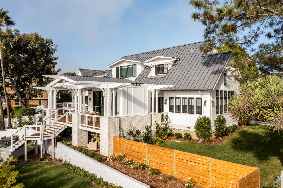 Foto della facciata di una casa grande bianca country a due piani con rivestimenti misti, tetto a capanna, copertura in metallo o lamiera e pannelli e listelle di legno