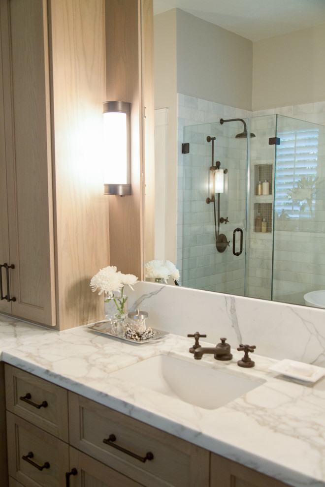 Inspiration for a mid-sized traditional master bathroom in Houston with an undermount sink, shaker cabinets, medium wood cabinets, marble benchtops, a freestanding tub, a corner shower, white tile, stone tile, grey walls and limestone floors.