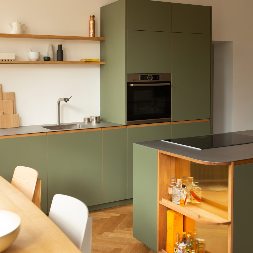 Design ideas for a mid-sized contemporary galley open plan kitchen in Berlin with a single-bowl sink, flat-panel cabinets, green cabinets, stainless steel benchtops, white splashback, stainless steel appliances, medium hardwood floors, with island and grey benchtop.