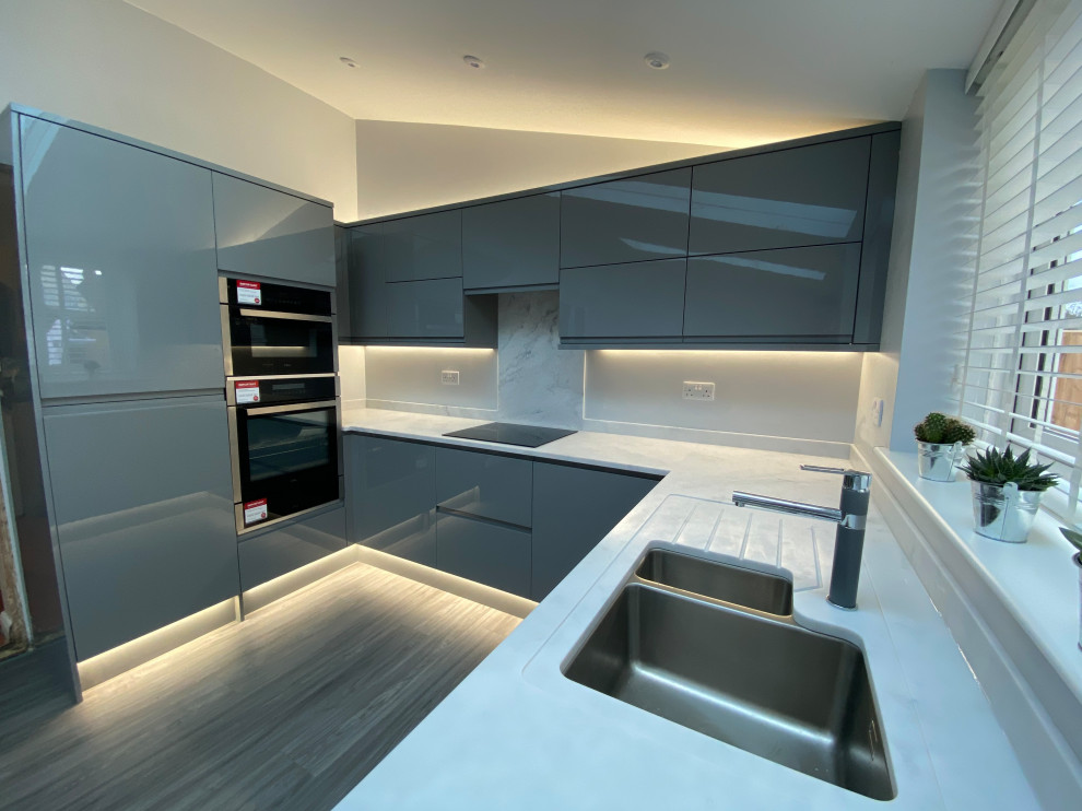 Inspiration for a large contemporary u-shaped open plan kitchen in Other with an integrated sink, flat-panel cabinets, grey cabinets, solid surface benchtops, white splashback, panelled appliances, vinyl floors, no island, brown floor, white benchtop and vaulted.