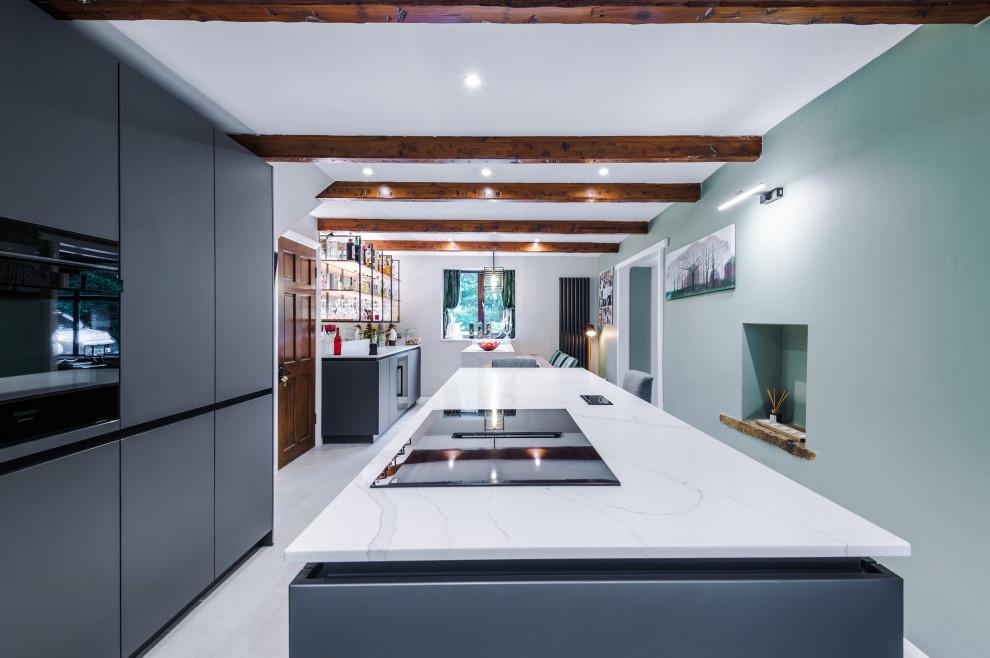 Photo of a mid-sized contemporary galley open plan kitchen in Manchester with a drop-in sink, flat-panel cabinets, grey cabinets, quartzite benchtops, glass sheet splashback, stainless steel appliances, with island and white benchtop.