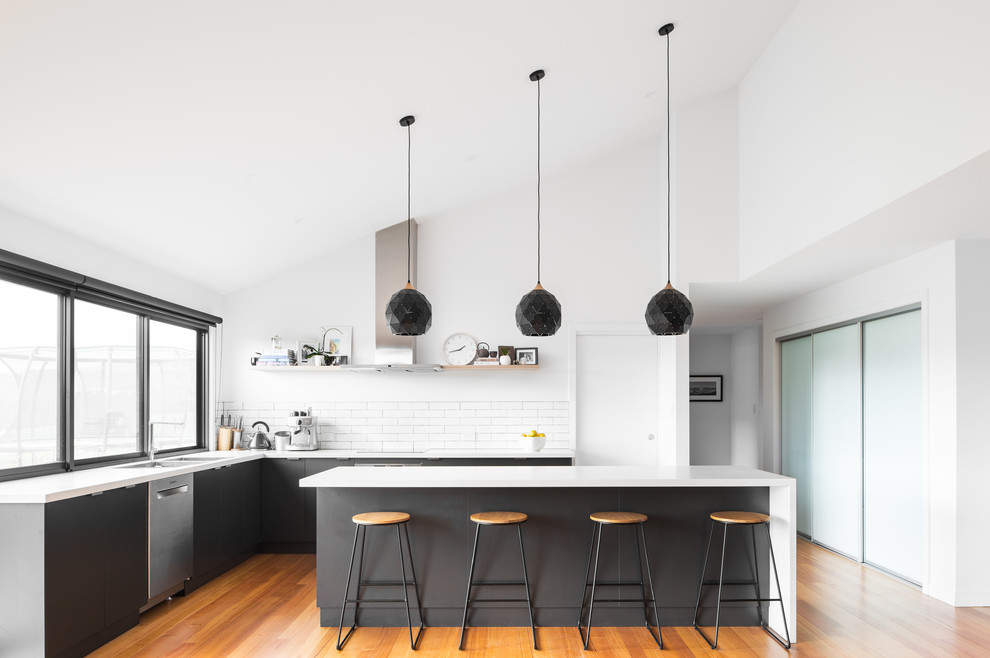 This is an example of a contemporary l-shaped kitchen in Hobart with an undermount sink, flat-panel cabinets, grey cabinets, white splashback, subway tile splashback, stainless steel appliances, medium hardwood floors, with island, brown floor and white benchtop.
