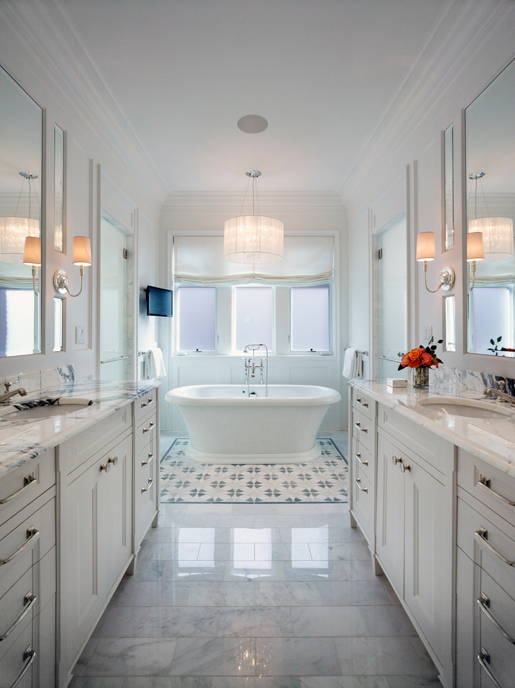 Photo of a large traditional master bathroom in Chicago with an undermount sink, white cabinets, marble benchtops, a freestanding tub, a two-piece toilet, gray tile, stone tile, white walls, marble floors and recessed-panel cabinets.