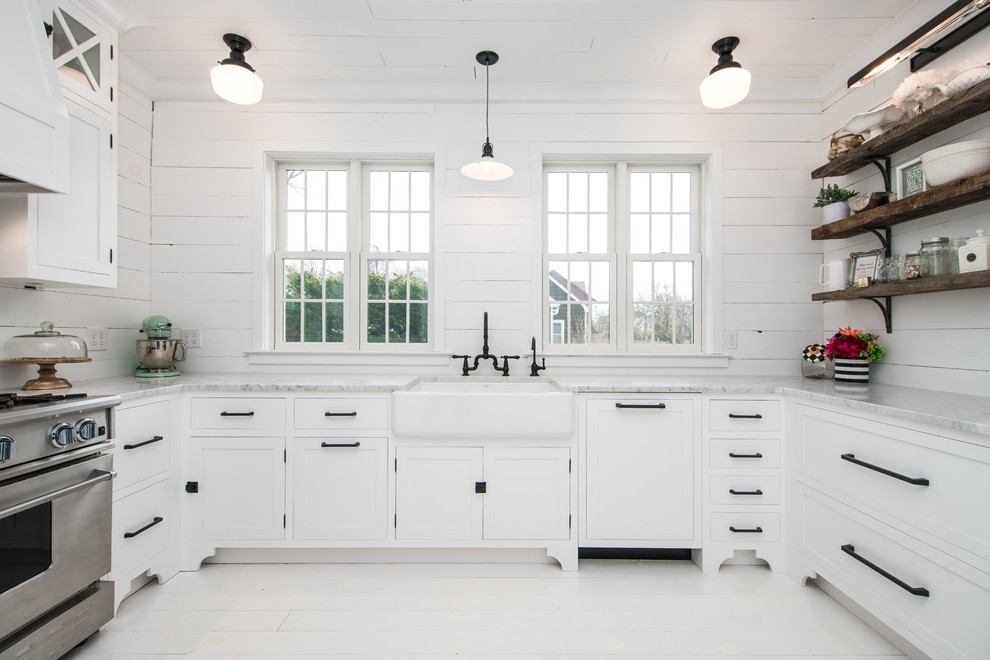 Photo of a mid-sized beach style u-shaped separate kitchen in New York with a farmhouse sink, shaker cabinets, white cabinets, marble benchtops, white splashback, timber splashback, painted wood floors, no island, white floor and stainless steel appliances.