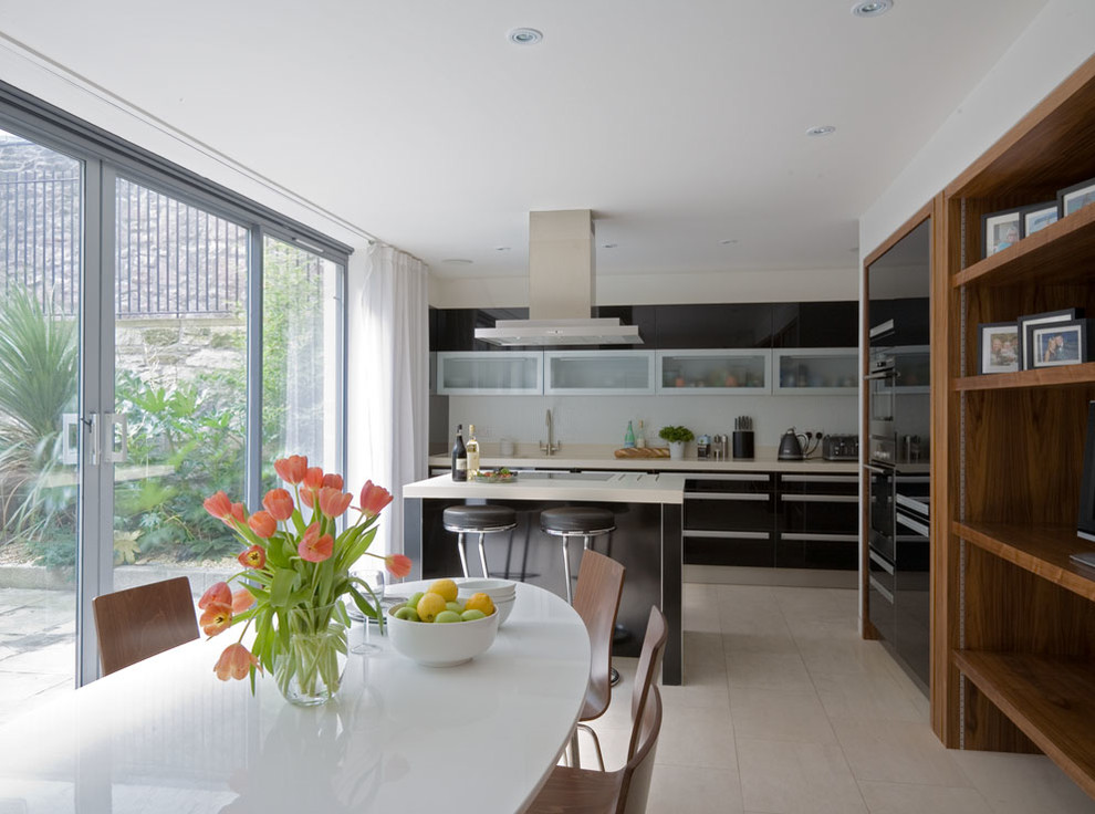 Photo of a mid-sized contemporary single-wall eat-in kitchen in Edinburgh with flat-panel cabinets, black cabinets, solid surface benchtops, white splashback, ceramic splashback, stainless steel appliances, porcelain floors and with island.